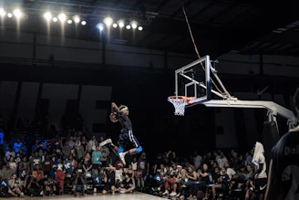 Action shot of Mazzi mid-air dunk during a high school basketball game, crowd cheering in the background.