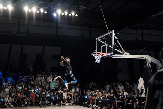 Action shot of Mazzi mid-air dunk during a high school basketball game, crowd cheering in the background.