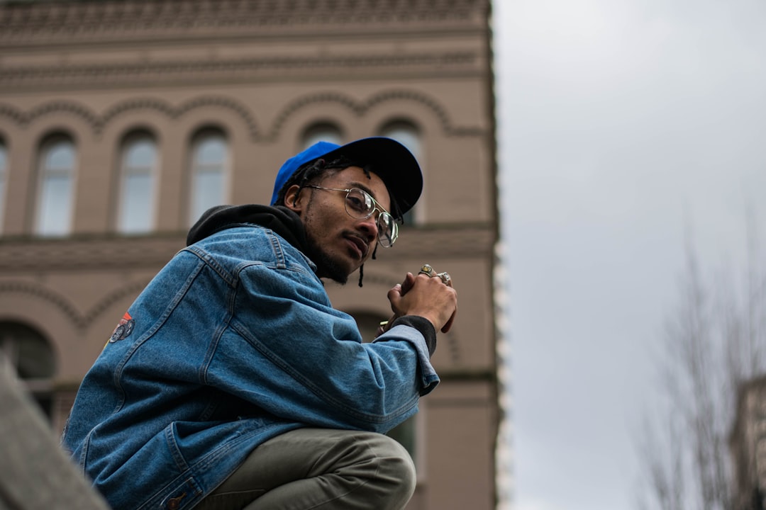 man wearing blue denim jacket and blue cap sitting outdoors