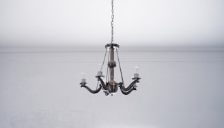 A vintage-style metal chandelier with five arms hangs from the ceiling. The chandelier has exposed bulbs and a bronze finish, set against a plain white ceiling and wall.