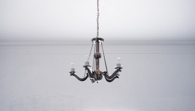 A vintage-style metal chandelier with five arms hangs from the ceiling. The chandelier has exposed bulbs and a bronze finish, set against a plain white ceiling and wall.