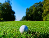 A close-up shot of a high-quality golf club striking a ball on a lush green fairway under bright sunlight.