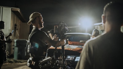 An outdoor night scene with cast and crew gathered under string lights, preparing for a low-budget feature film take.