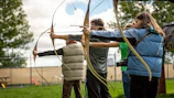 Shooters lined up in traditional tweed jackets aiming at clay targets