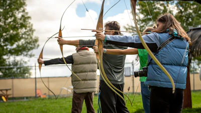 A group of serious shooters gathered around, discussing crossbow tech outdoors.