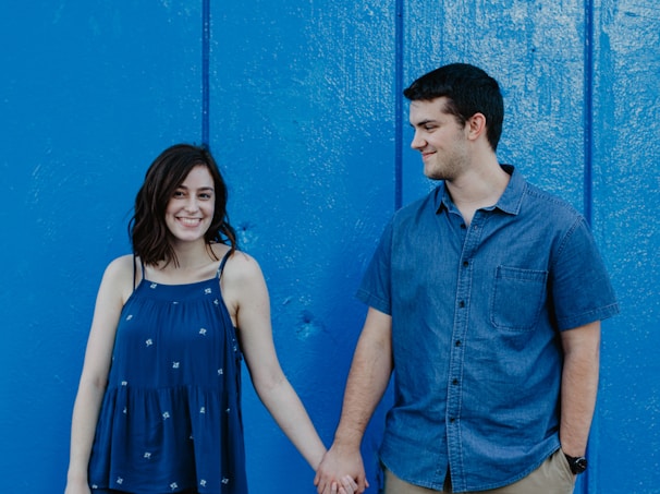 A stylish couple sharing a lighthearted moment, dressed casually with blue and orange tones in the background.