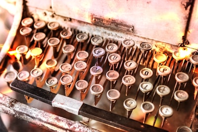 An antique typewriter with round keys arranged in neat rows, featuring letters and numbers. The metal frame shows signs of vintage wear, and warm lighting creates a nostalgic atmosphere.
