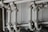 A series of interconnected industrial pipes with visible joints and flanges. The pipes have a worn, matte texture and are arranged in a horizontally aligned, organized manner. The background is an industrial setting, possibly a basement or maintenance area, with a neutral color palette.
