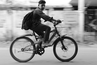 A young person rides a bicycle quickly, creating a sense of motion blur in the background. They carry a backpack and seem to be focused on the path ahead.