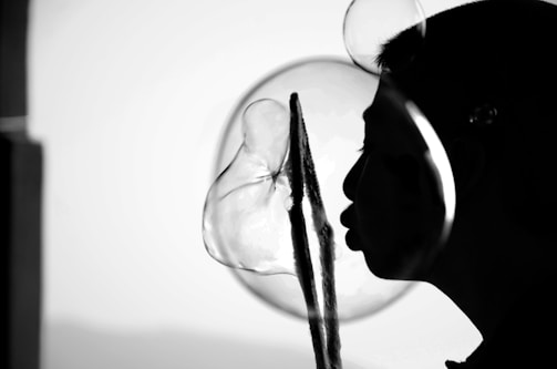 A silhouette of a person is blowing bubbles, with a large bubble prominently visible against a light background. The bubbles' reflections and transparency create interesting visual effects.