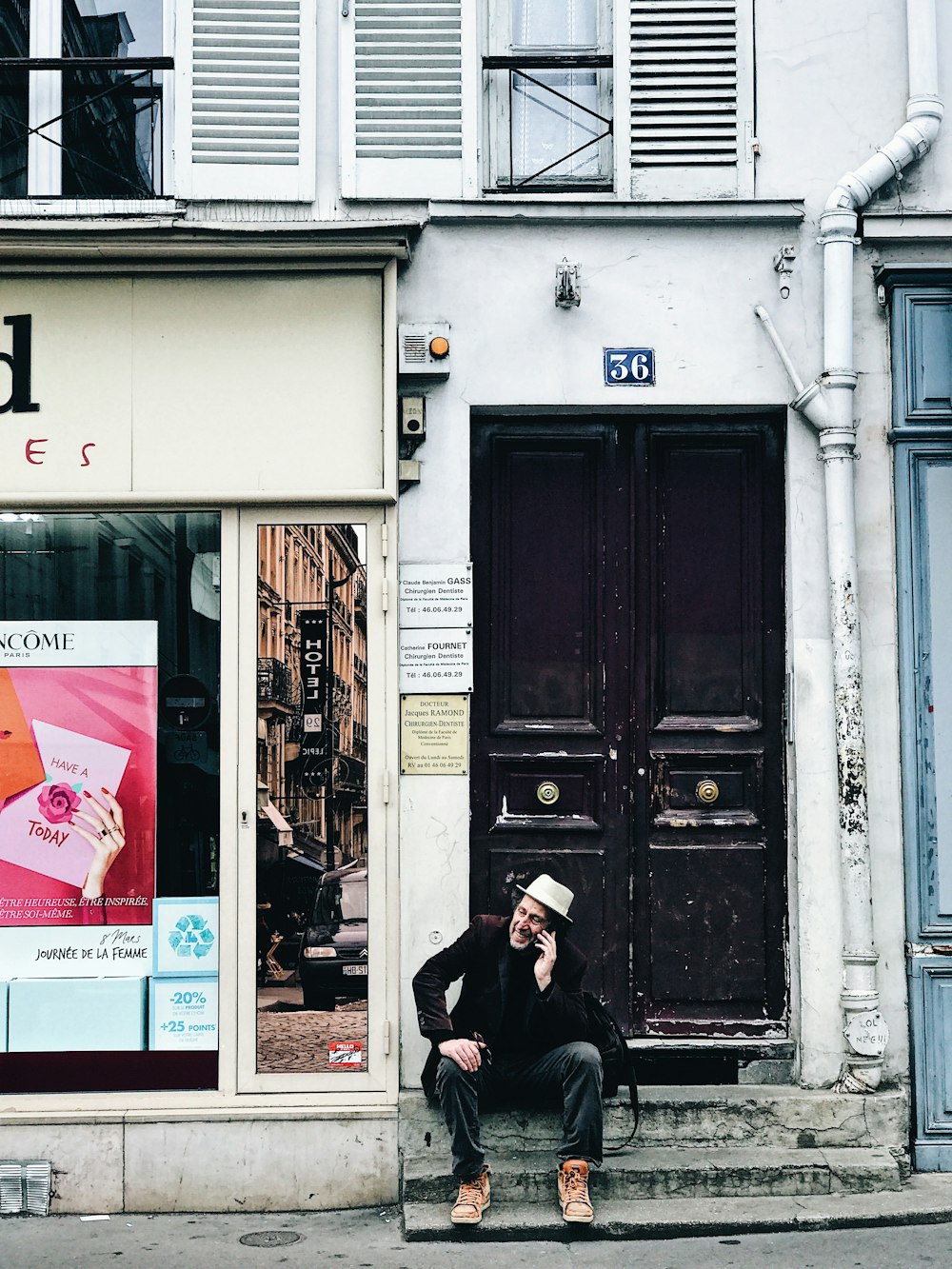 man sitting outside door while calling using smartphone during daytime