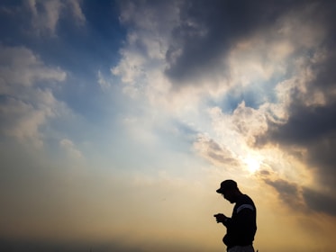A dramatic silhouette of a person standing strong against a dark sky with rays of light breaking through.