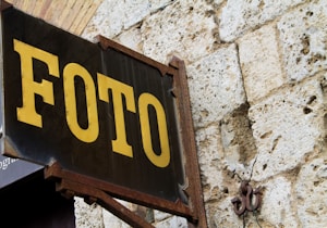 A vintage sign with the word 'FOTO' in large yellow letters is mounted on an old stone wall. The sign has a dark background and ornate metal brackets.