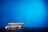 A laptop is partially open on a dark surface with its screen displaying a webpage. The backdrop is a vibrant blue, creating a contrast with the darker tones of the laptop.