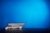 A laptop is partially open on a dark surface with its screen displaying a webpage. The backdrop is a vibrant blue, creating a contrast with the darker tones of the laptop.