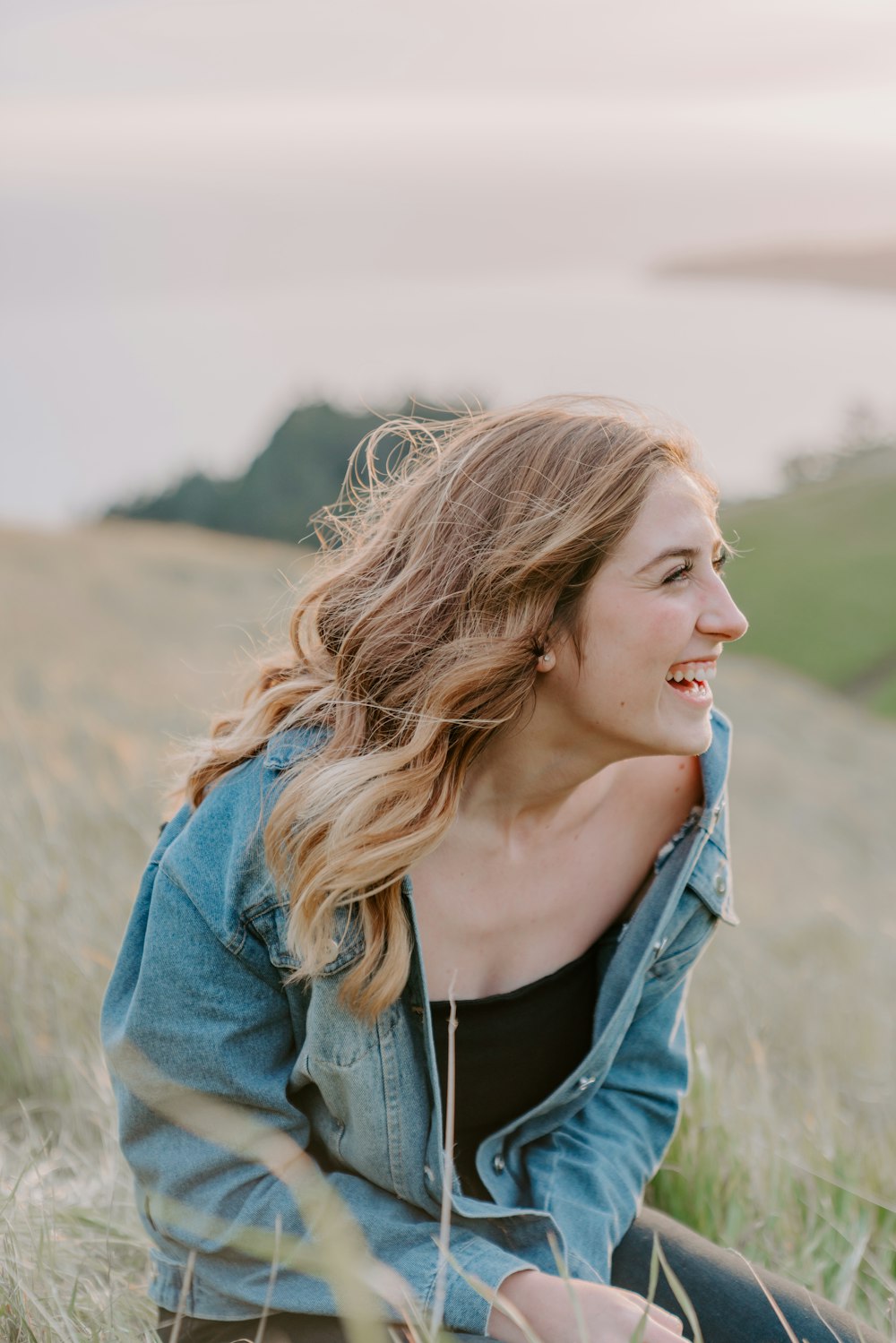 a woman sitting in a field with her hair blowing in the wind