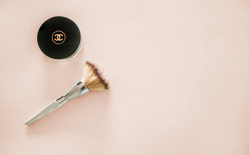 makeup brush and Chanel compact jar on beige surface