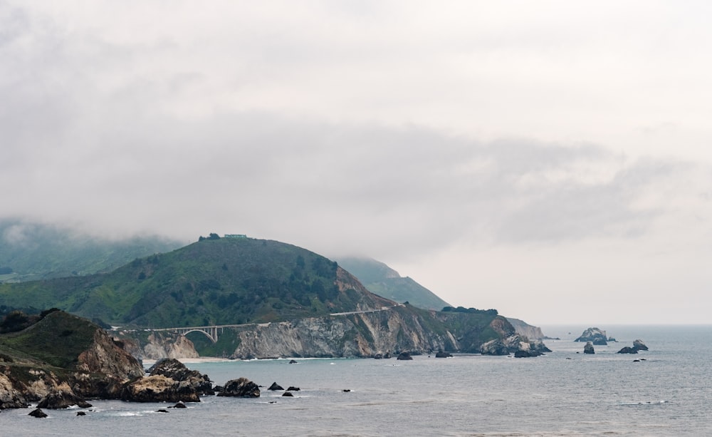 ocean near mountain under cloudy sky