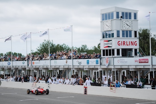 Crowd cheering at a vintage car race track under bright sunny skies.