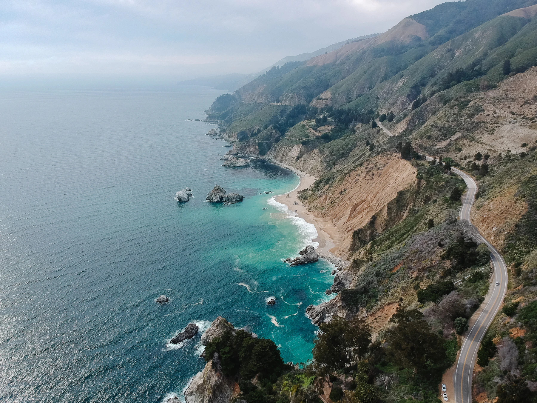 Aerial view of Highway 1 along Big Sur cliffs above turquoise water