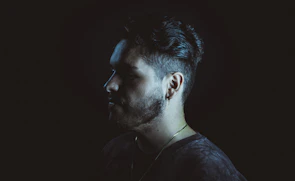Close-up of a stylish male profile highlighting a tailored haircut and defined beard edges with subtle golden highlights.