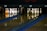 A dimly lit bowling alley with two lanes is depicted, featuring sets of bowling pins arranged neatly at the end of each lane. An orange bowling ball rests on the left lane, while a brown bowling ball is visible on the right. The wooden lanes reflect the pins and balls slightly, adding depth to the scene.