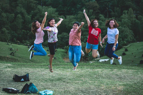 five women jumping on green grass