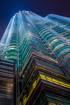 A sleek, modern skyscraper bathed in emerald green and champagne gold light against a deep royal navy blue sky, symbolizing global investment and progress.
