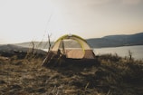 A lightweight tent pitched on a grassy hilltop overlooking a mountain range at sunrise.
