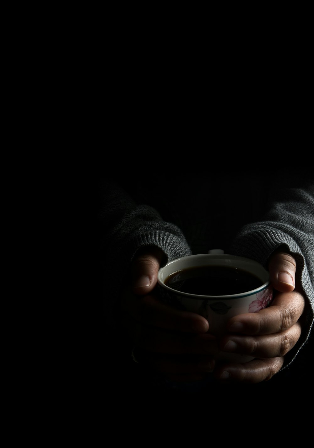 person in grey sweater holding cup with both hands