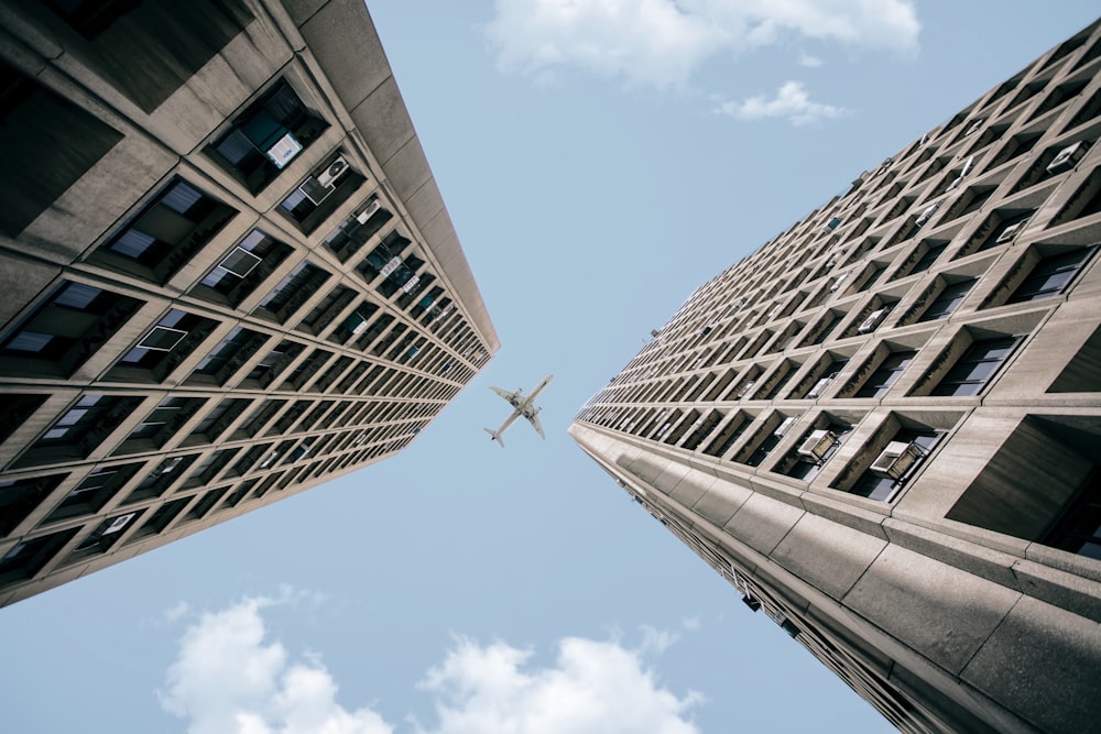 낮에 두 개의 고층 건물을 가로지르는 비행기의 로우 앵글 사진
