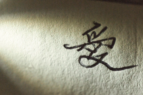 Close-up of textured paper with deep black ink forming abstract poetic lines under soft directional light