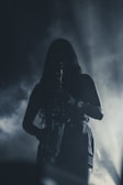 A silhouette of a person playing a saxophone, surrounded by fog or smoke. The lighting creates a dramatic and mysterious atmosphere with a focus on the saxophone.