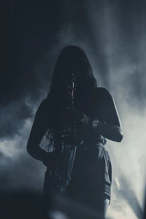 Silhouette of Adrian Sorel holding a saxophone, backlit by soft, glowing amber light in a darkened room.