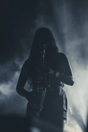 Silhouette of Adrian Sorel holding a saxophone, backlit by soft, glowing amber light in a darkened room.