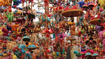 A vibrant display of traditional handcrafted hanging ornaments featuring colorful animal shapes, decorative umbrellas, and beaded strings. The intricate designs are rich in detail, with a variety of textures and materials used to create a visually striking scene.