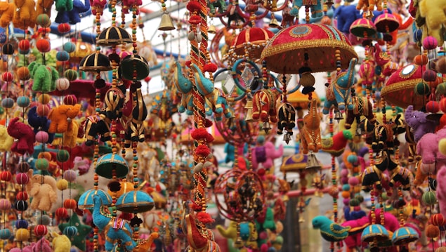A vibrant display of traditional handcrafted hanging ornaments featuring colorful animal shapes, decorative umbrellas, and beaded strings. The intricate designs are rich in detail, with a variety of textures and materials used to create a visually striking scene.