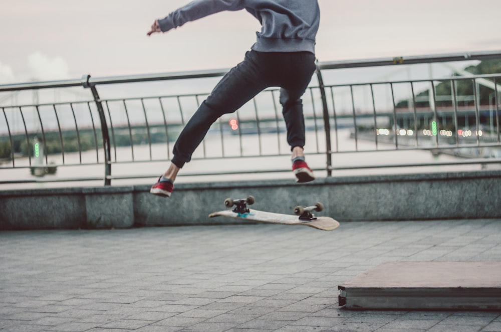 selective focus photography of person about to flip above using skateboard near railway and body of water