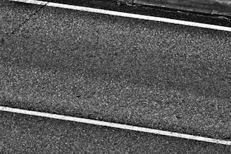 Two white parallel lines on a dark asphalt road surface with a rough texture.