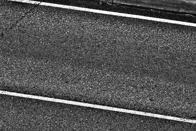 Two white parallel lines on a dark asphalt road surface with a rough texture.