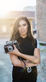Black-and-white portrait of a photographer holding a vintage camera amidst natural outdoor lighting.