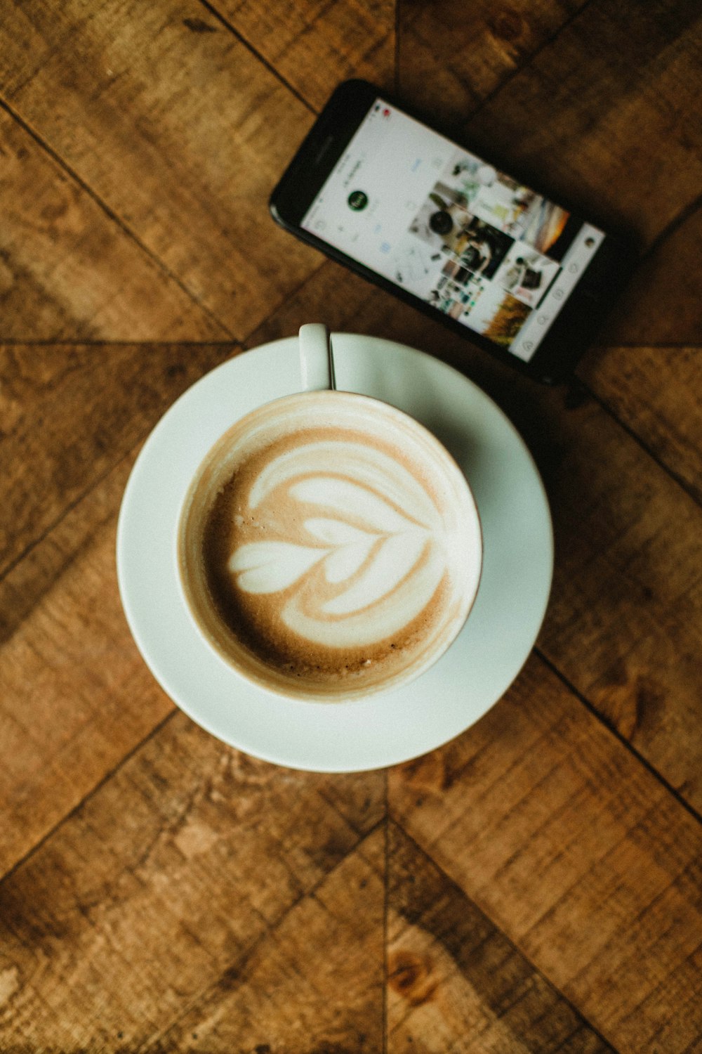 Cappuccino auf Untertasse neben dem iPhone