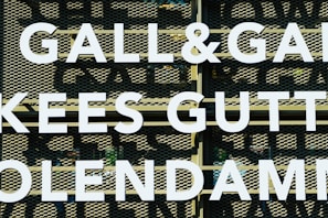 Large white letters spell out 'GALL&GALL' and 'KEES GUTT' against a perforated metal background. The letters appear to be part of an outdoor sign or billboard.