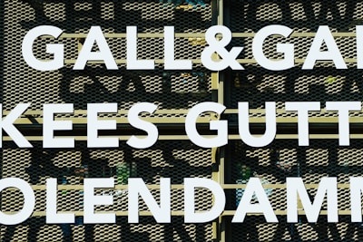 Large white letters spell out 'GALL&GALL' and 'KEES GUTT' against a perforated metal background. The letters appear to be part of an outdoor sign or billboard.