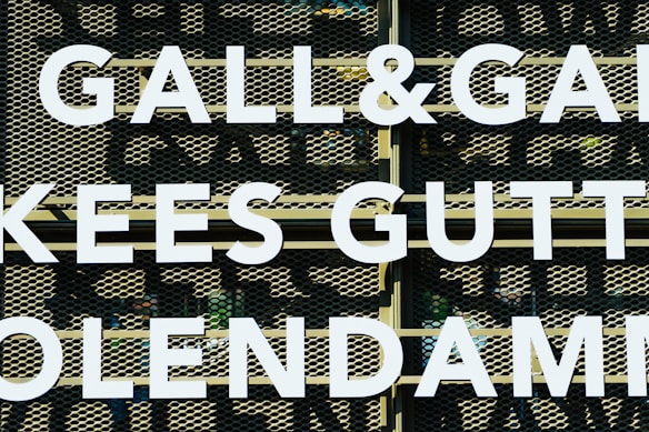 Large white letters spell out 'GALL&GALL' and 'KEES GUTT' against a perforated metal background. The letters appear to be part of an outdoor sign or billboard.
