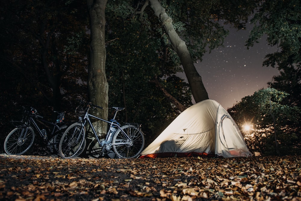흰색 캠핑 텐트와 키 큰 나무 근처의 검은 색과 회색 자전거