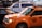 A yellow taxi is parked on the street, reflecting the bright lights of the surrounding urban environment. Nearby is an NYPD police vehicle, indicating a busy city setting.