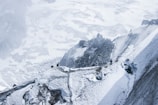 A group of climbers traverses a narrow, snowy ridge with steep cliffs. The expansive backdrop displays a rugged mountainous landscape covered in snow and ice. The scene conveys a sense of adventure and challenge.