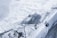 A group of climbers traverses a narrow, snowy ridge with steep cliffs. The expansive backdrop displays a rugged mountainous landscape covered in snow and ice. The scene conveys a sense of adventure and challenge.