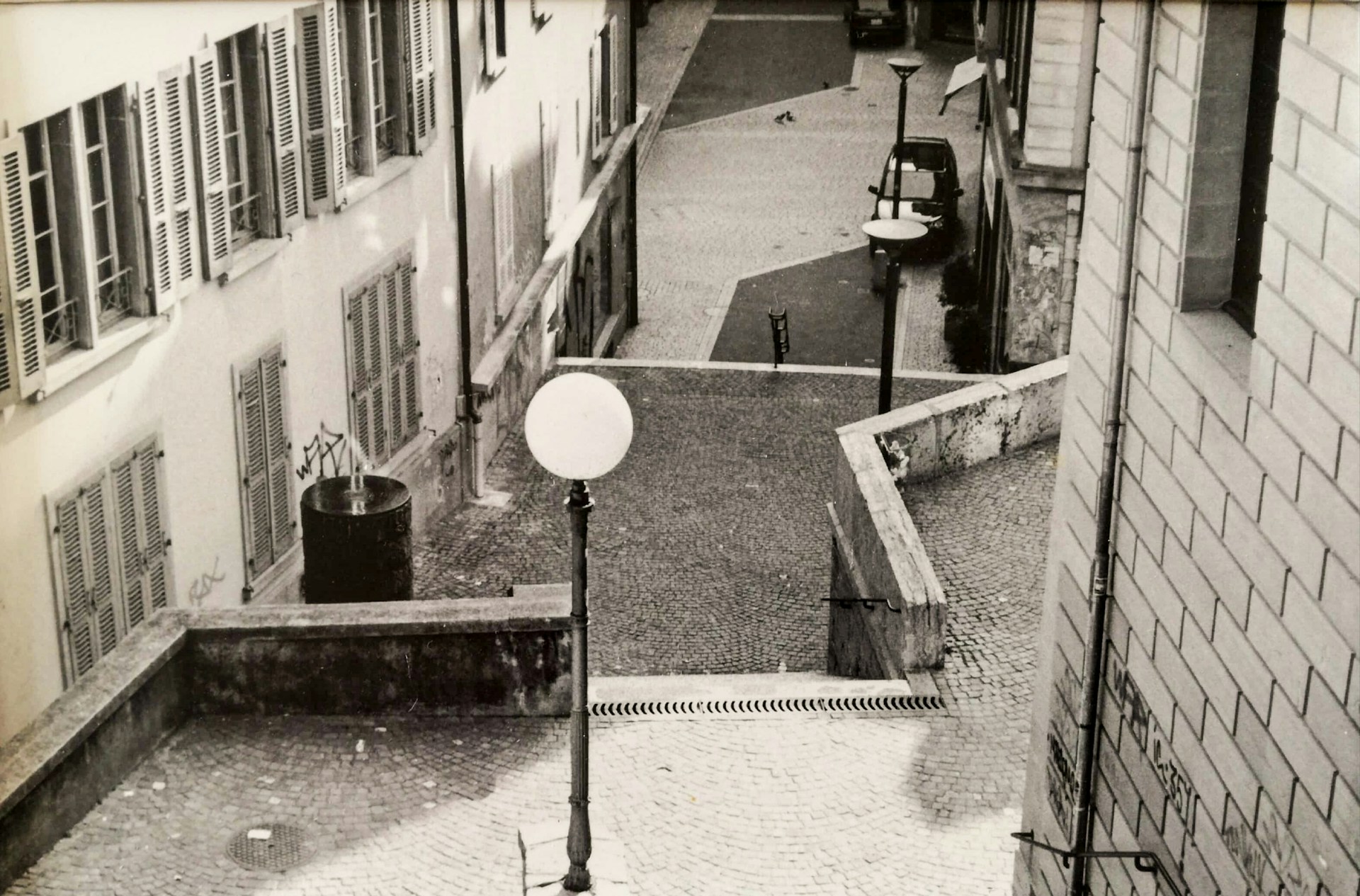 Black and white street photograph capturing a quiet moment in a narrow alley of Genoa, with elegant shadows playing on the cobblestones.
